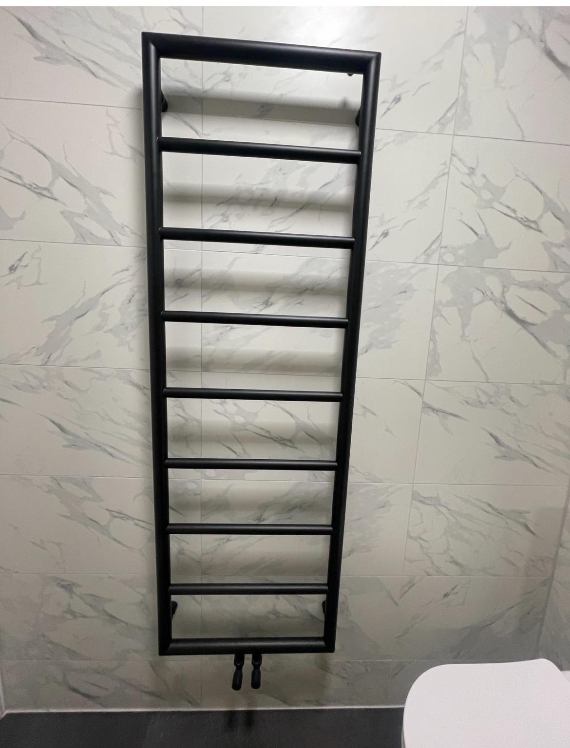 Black towel radiator against marble-effect wall